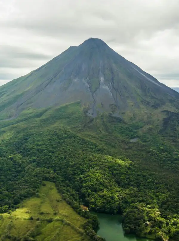 Dramatic aerial view of the lush green Arenal Volcano in Costa Rica against a cloudy sky.